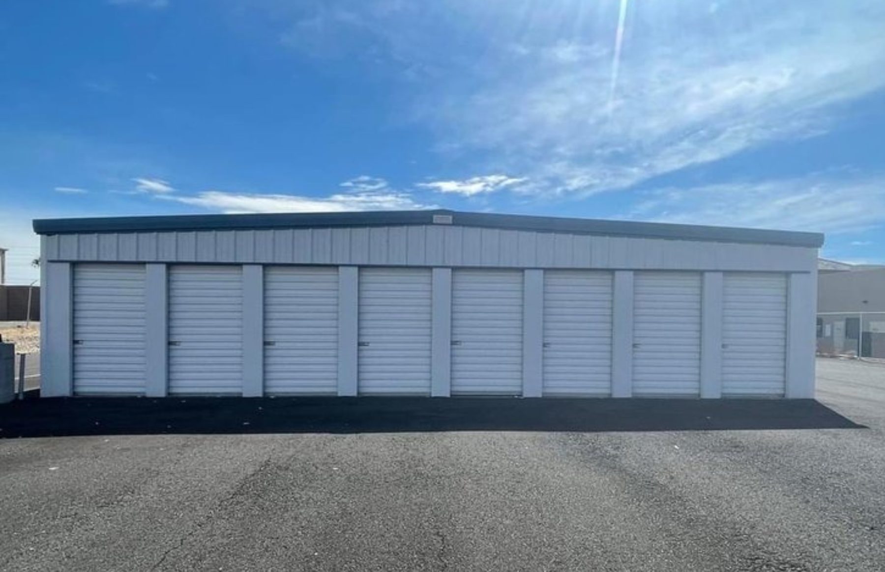 Full view of the PDMV1 Storage building, a long metal structure with eight white roll-up doors facing a freshly paved apron