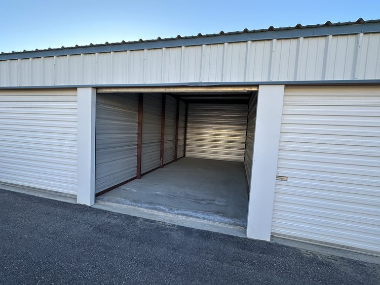 Drive-up unit at PDMV1 Storage with the roll-up door raised, showing a swept concrete floor and steel walls